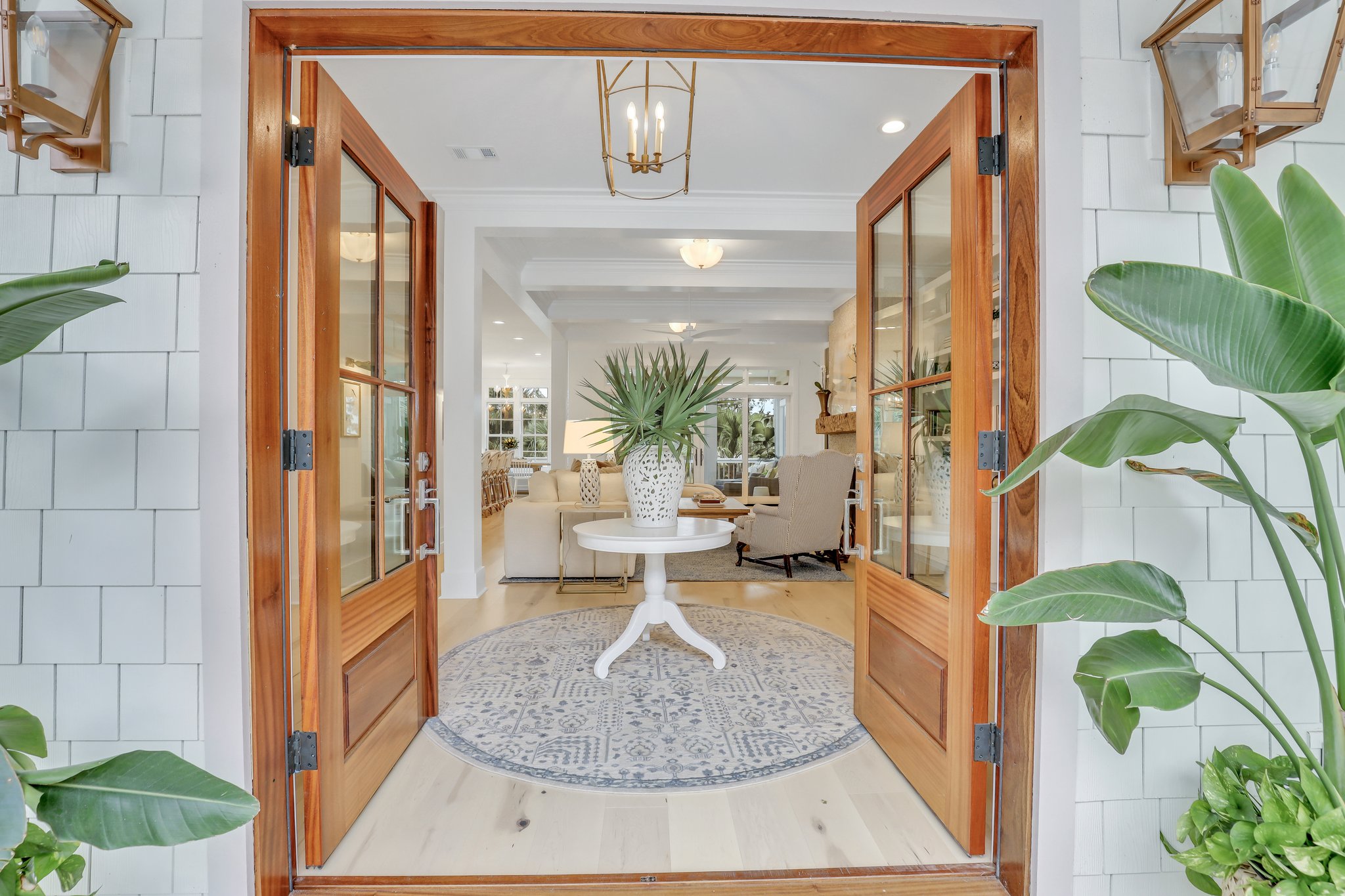 Medium-toned, stained wood double front doors with four lights welcome you home to this low country-inspired coastal cottage home outside of Savannah on the riverfront of South Georgia